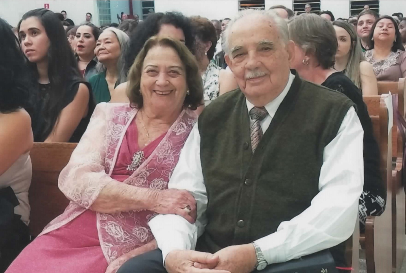 Antenor e Maria, já idosos, sorrindo sentados lado a lado em um culto.