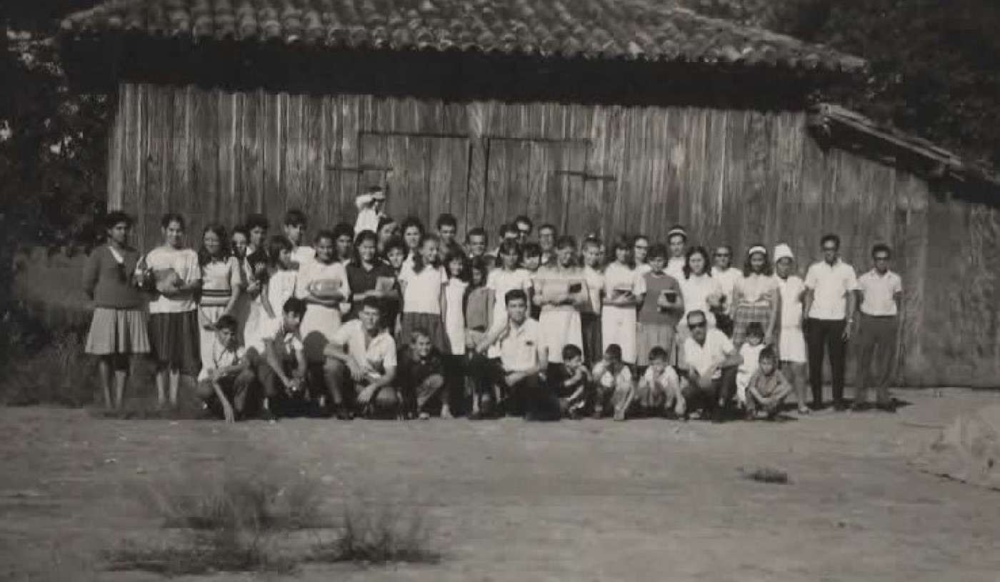Grande grupo de crianças e jovens segurando Bíblias em frente a um galpão de madeira, em foto antiga.