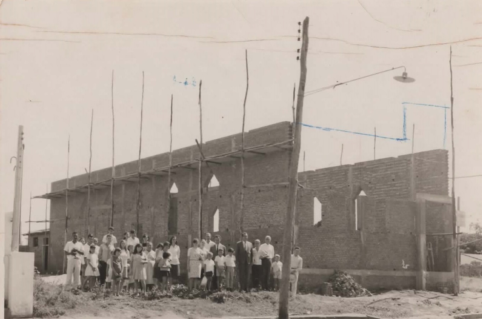 Congregação posando em frente ao templo em construção, com andaimes de madeira, em foto antiga.