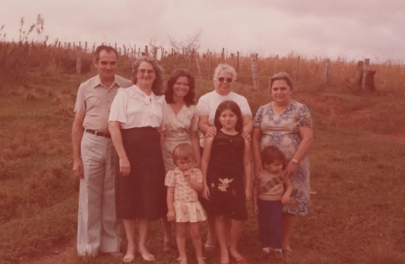 Família reunida em um campo, em fotografia antiga de tom avermelhado.