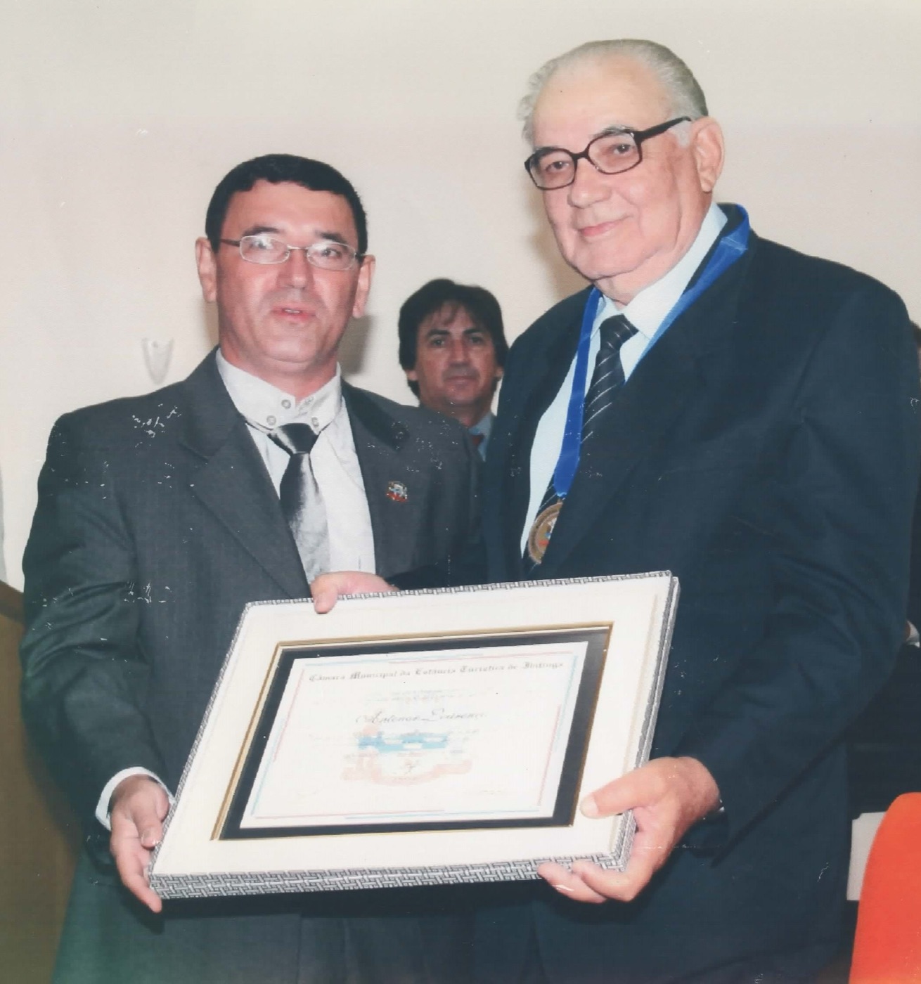 Pr. Antenor, com medalha ao pescoço, recebendo o certificado emoldurado da Câmara Municipal.
