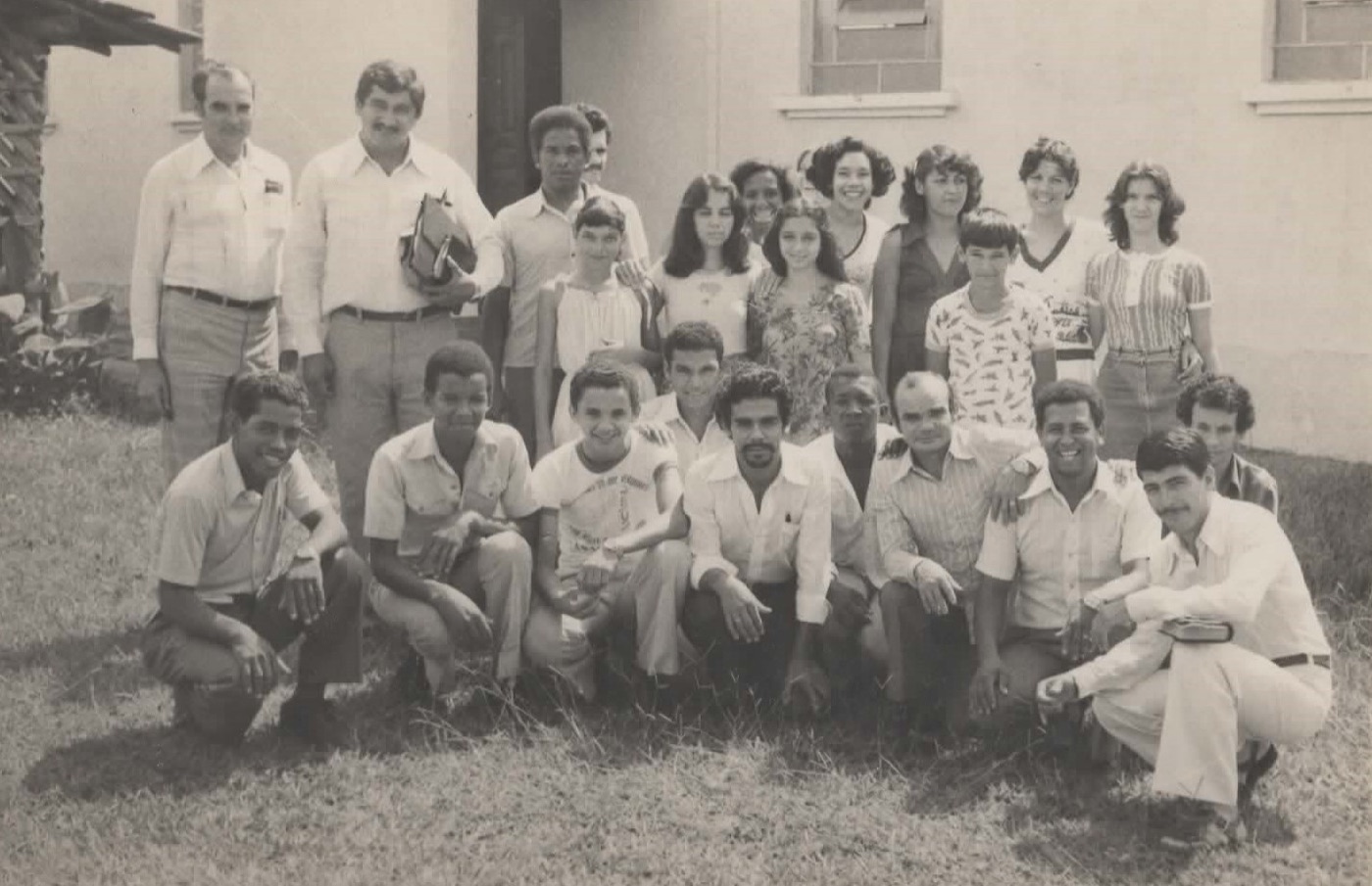 Jovens da igreja reunidos e sorridentes em frente a uma casa branca, em foto antiga.